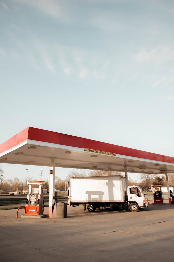A delivery truck refueling at an outdoor gas station under a clear blue sky.